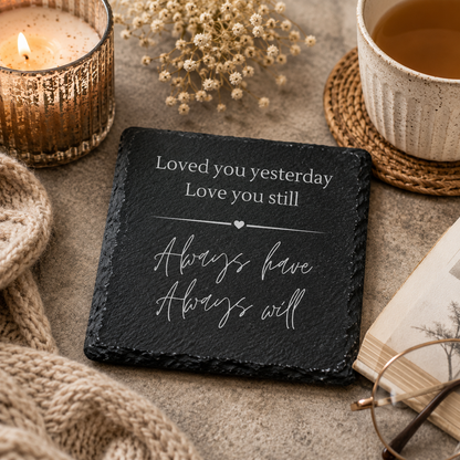 Slate coaster with romantic quote, candle, cup of tea, and dried flowers on a textured surface.