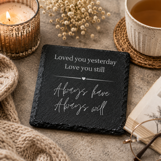 Slate coaster with romantic quote, candle, cup of tea, and dried flowers on a textured surface.