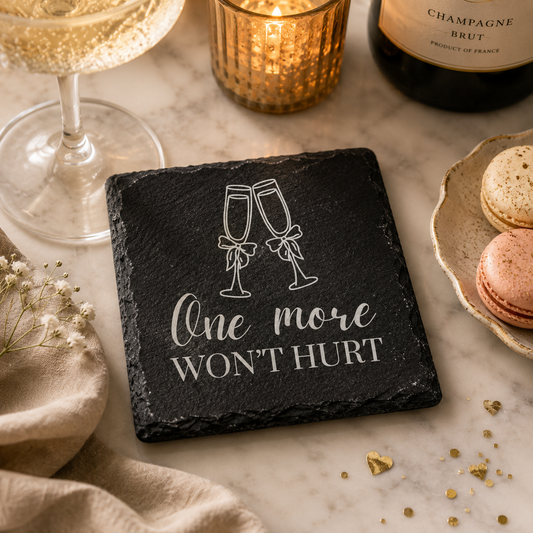 Slate coaster with champagne glasses and text on a marble surface with wine glass, candle, and macarons.