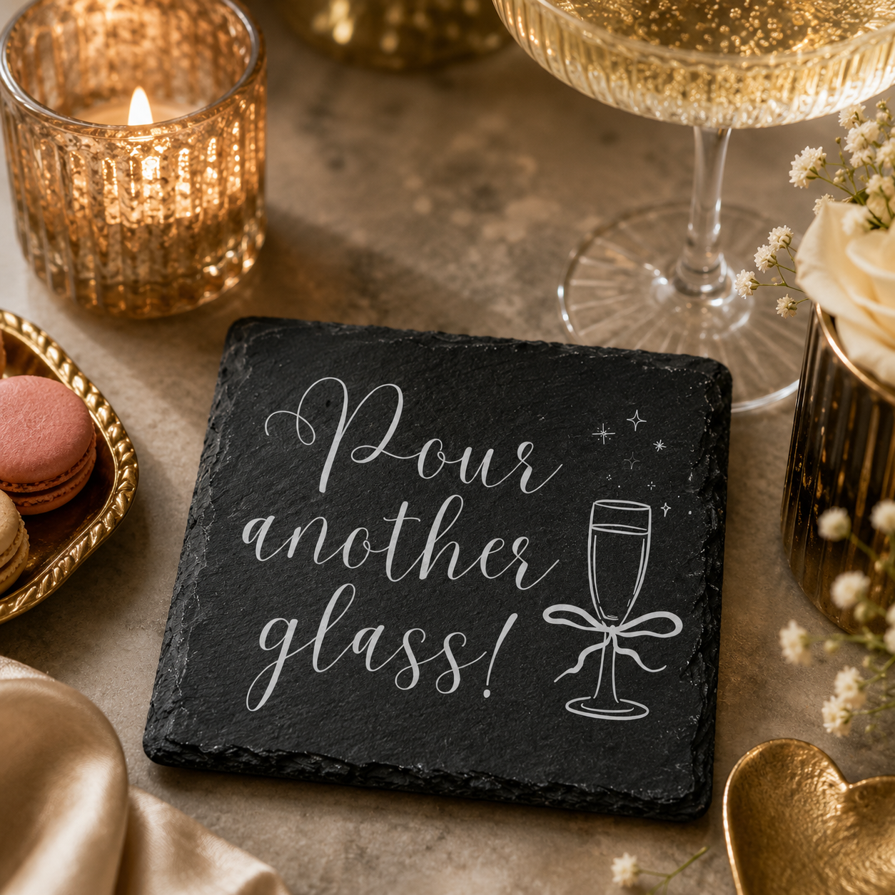 Slate coaster with 'Pour another glass!' text on a table with wine glasses, candles, and macarons.