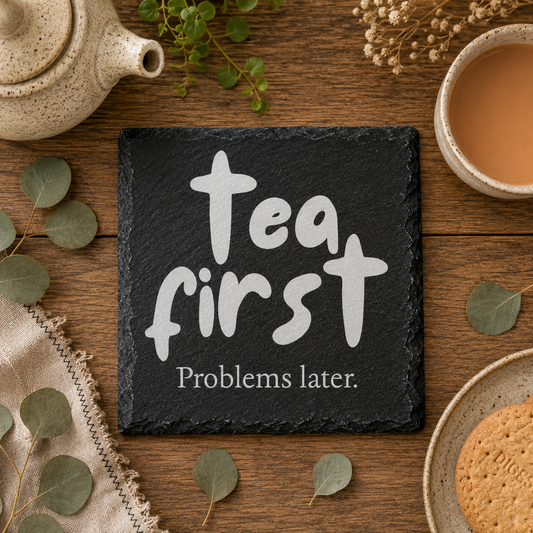 Tea first problems later slate coaster on a wooden table with tea and cookies.