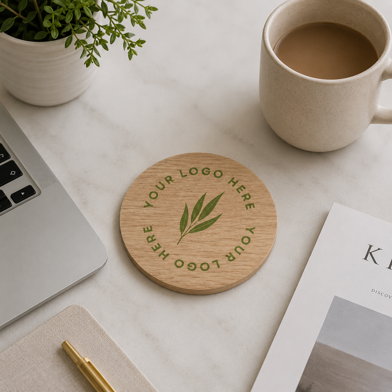 A round wooden coaster with custom logo, displayed on a light marble desk with a laptop, coffee mug, notebook, and plant.