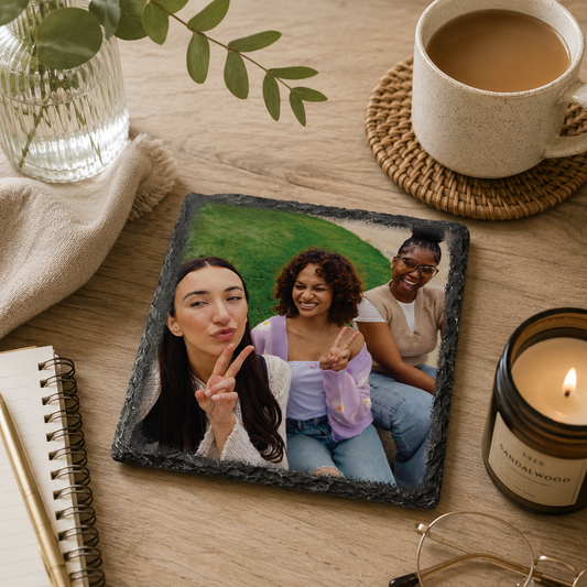 Personalised slate photo coaster with three friends on a wooden table with a cup of coffee, candle, and notebook.